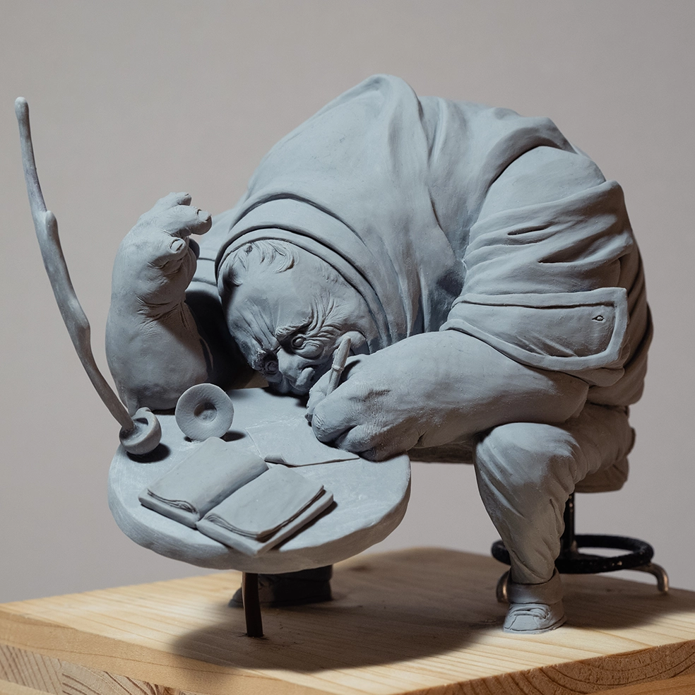 Sculpture by artist Teddy Ros "Café-Créa" 2022, sculpted in polymer clay, depicting a large character sitting on a stool writing in a small notebook, while his coffee cup shatters. Teddy Ros is a contemporary art artist.